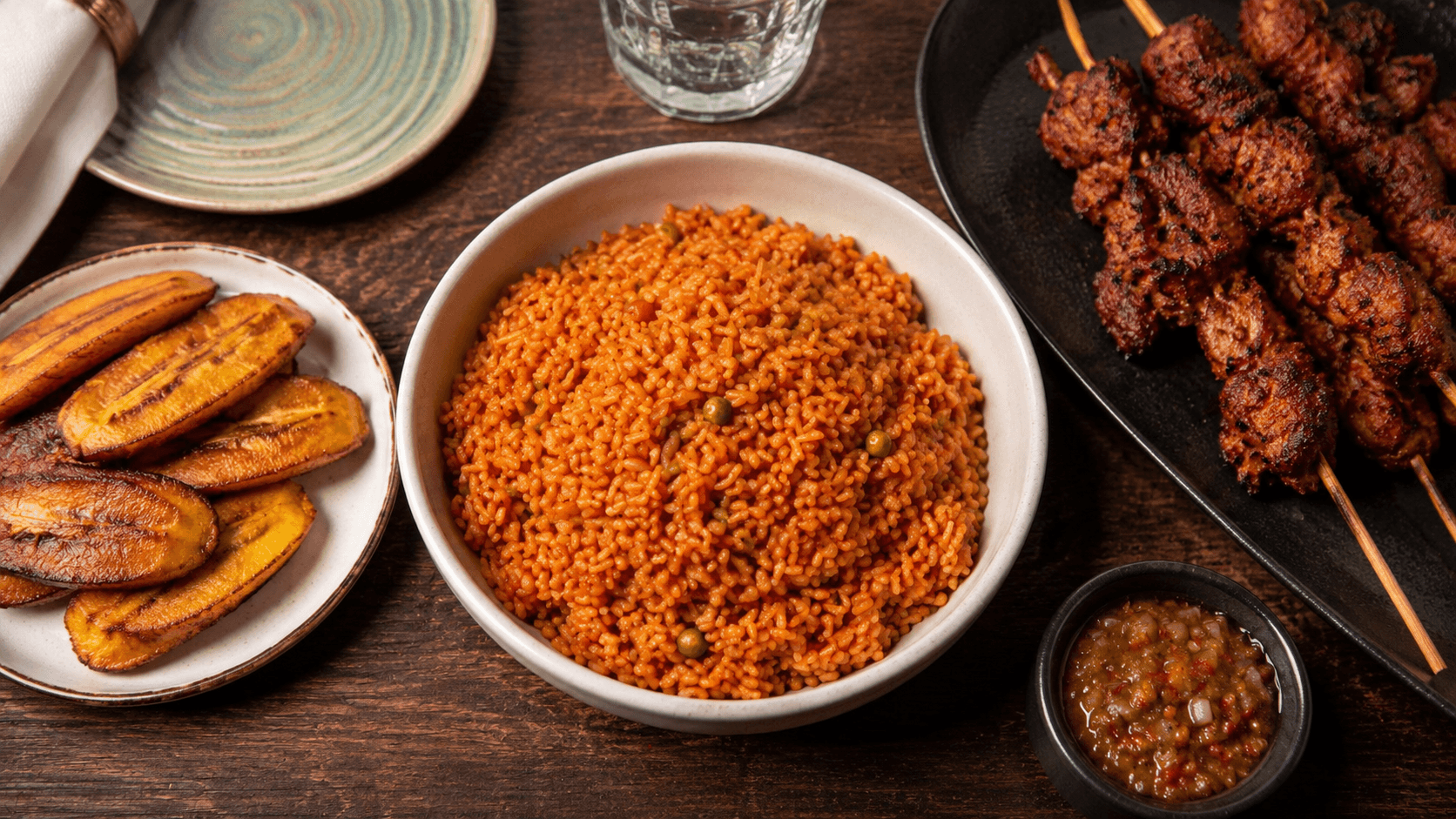 A spread of Hot N Nice home-cooked dishes including jollof rice, plantain lasagna, suya skewers and soups